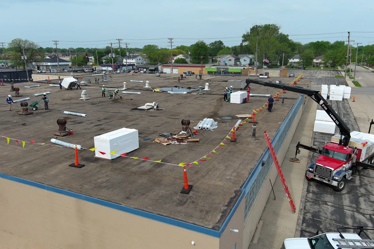 Aerial drone view of Americanstruction crew installing insulation on a large flat industrial warehouse roof in Racine, Wisconsin
