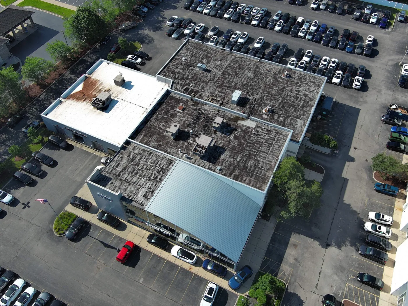 Failing modified bitumen roof on Audi Orland Park dealership before recover, front-right drone elevation